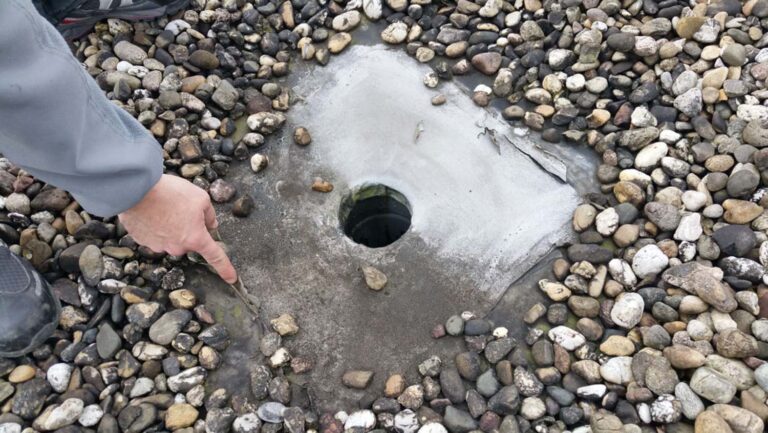 Mensch zeigt auf Dachabfluss mit Kies