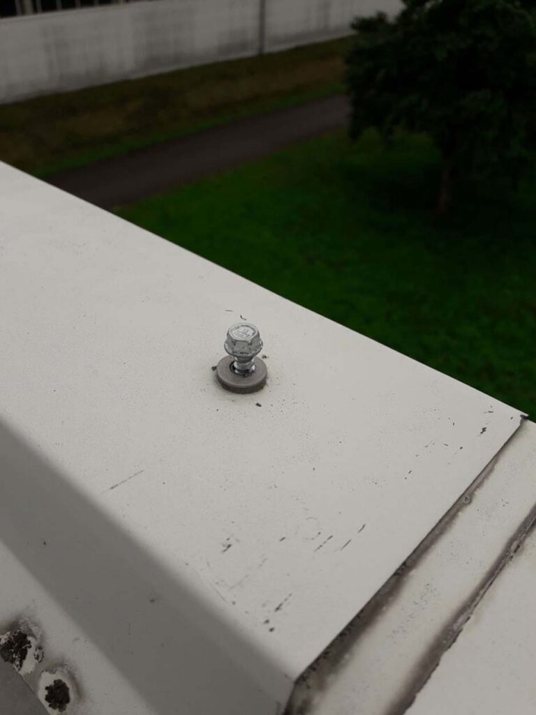 Schraube auf weißem Metall, grüner Rasen im Hintergrund.