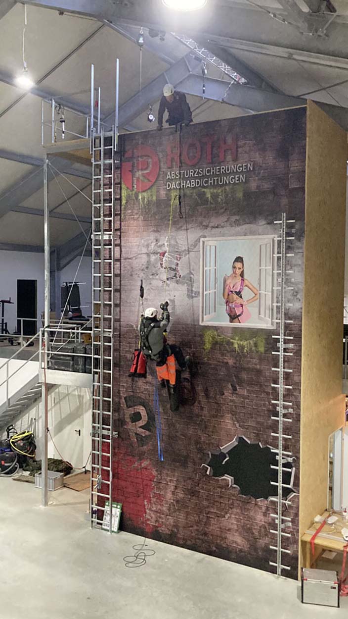 Person klettert an Sicherheitswand mit Gerüst und Leiter.