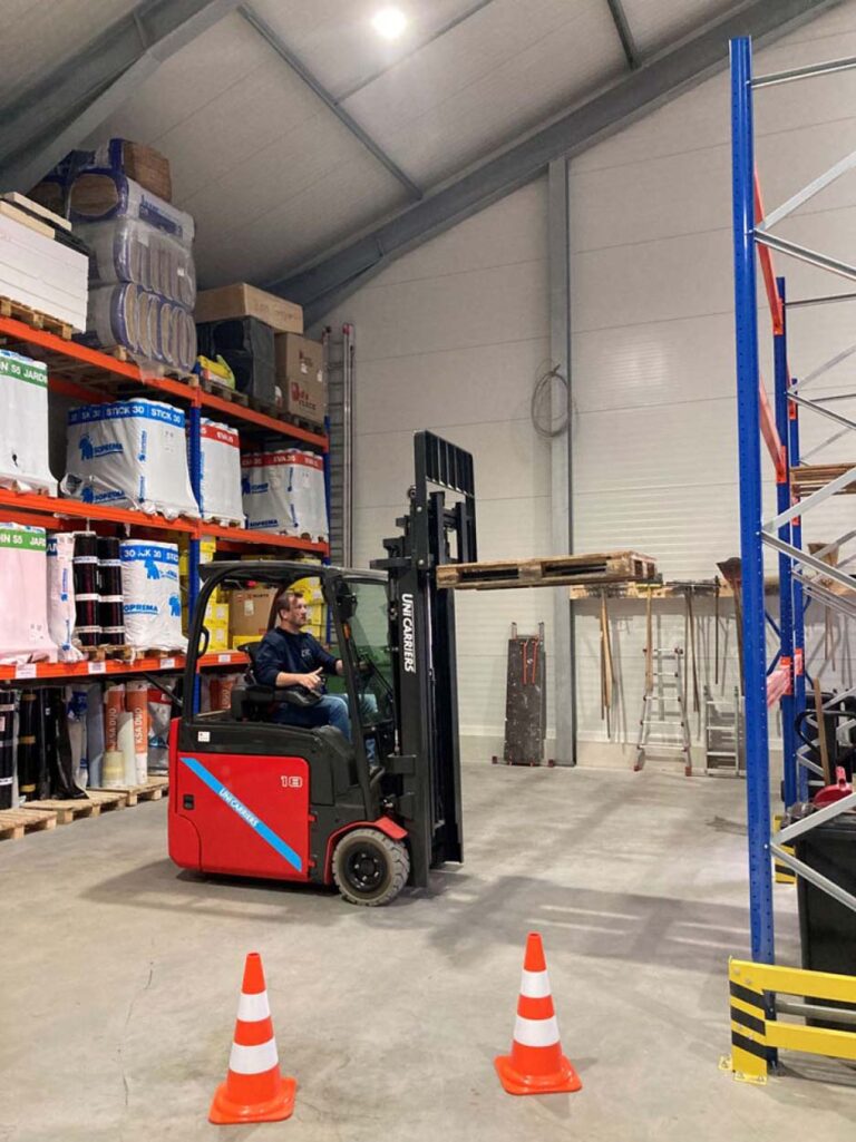 Gabelstaplerfahrer im Lager zwischen Regalen und Pylonen.