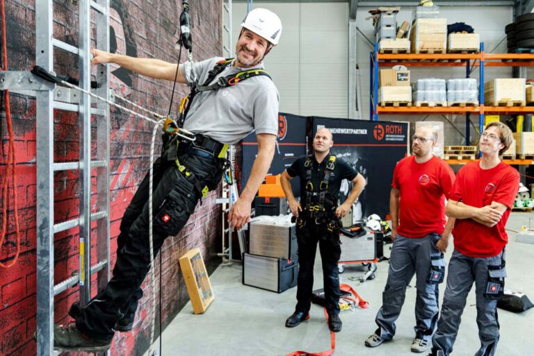 Mann auf Leiter mit Sicherheitsausrüstung in einer Halle.