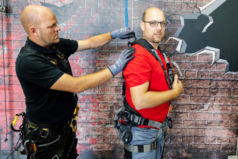 Zwei Männer mit Sicherheitsausrüstung vor Ziegelwand.