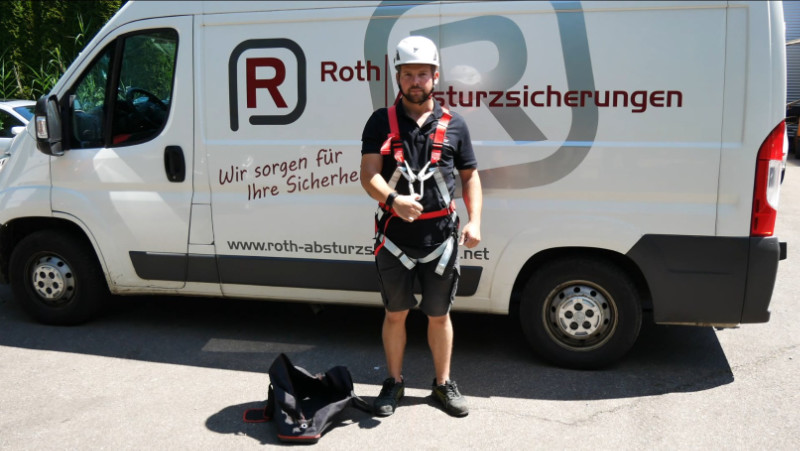 Person mit Sicherheitsausrüstung vor Firmenfahrzeug