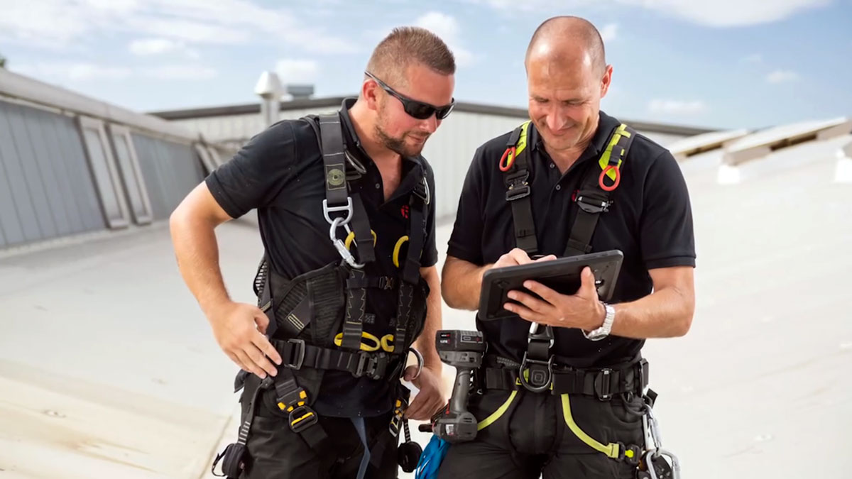 Zwei Männer analysieren Tablet auf Dach.